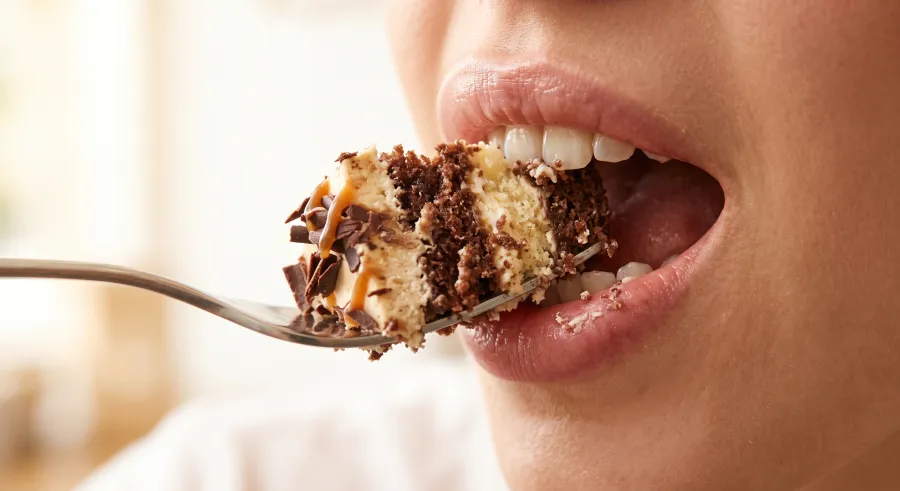 Mulut terbuka menyantap potongan kue cokelat di atas garpu